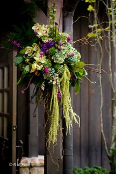 an arrangement of flowers is hanging from a pole in front of a wooden wall and fence