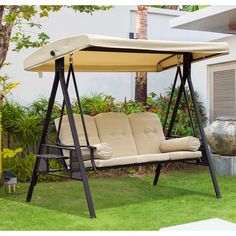 a swing chair with a canopy over it on the grass in front of a house