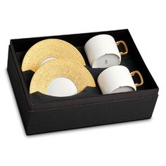 a black box with three white and gold plates in it, two cups and one saucer