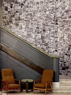 two chairs sitting next to an escalator in front of a wall covered with newspaper