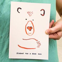 a person holding up a card with a bear drawn on it that says, sending you a bear hug