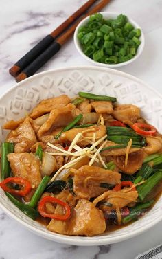 a white bowl filled with chicken and veggies next to chopsticks on a table