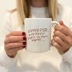 a woman holding a white coffee mug with red writing on the bottom and brown lettering that says, every good is perfect gift is from above