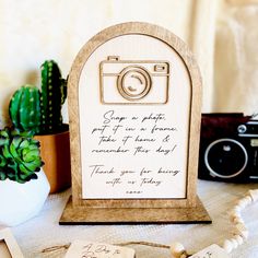 a wooden sign with a camera on it sitting next to a potted plant and other items