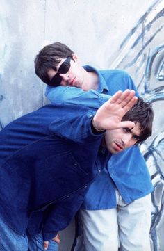 two young men leaning against a wall with their hands on each other's shoulders