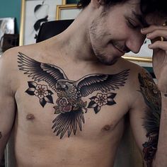 a man with an eagle tattoo on his chest holding a cell phone to his ear