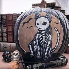 a pumpkin with a cat painted on it sitting next to some books and other halloween decorations