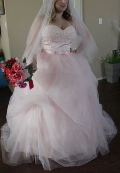 a woman in a pink wedding dress and veil holding a red rose bouquet standing next to a doorway