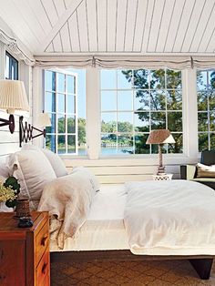 a bedroom with white walls and windows overlooking the water