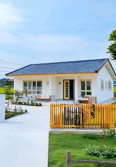 a small white house with a blue roof and wooden fence in front of the yard