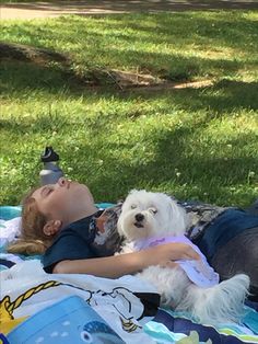 a woman laying on top of a blanket next to a white dog in a park