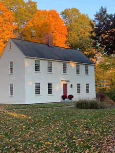 a large white house sitting on top of a lush green field next to trees with orange leaves