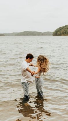 a man and woman standing in the water holding each other's hands as they hug