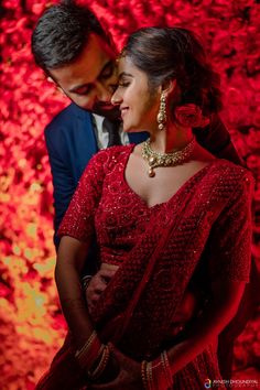 a man and woman standing next to each other in front of a red wall with flowers