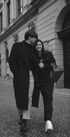 a man and woman are walking down the street in black and white, smiling at each other