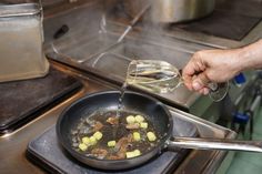 a person pouring water into a frying pan filled with food on top of a stove