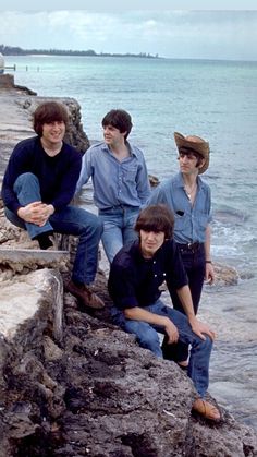 four young men are sitting on the rocks by the water and posing for a photo