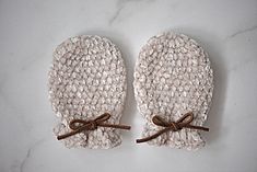 two white mittens with brown bows on top of a marble countertop next to each other