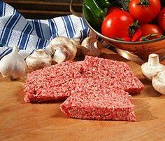 raw meat and vegetables on a cutting board next to a bowl of tomatoes, mushrooms, garlic