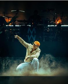 a man in white pants and an orange hat on stage with his arms out to the side