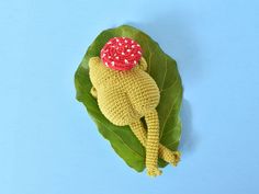 a crocheted toy laying on top of a green leaf with a red flower