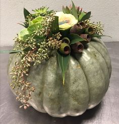 a green pumpkin filled with lots of flowers and greenery sitting on top of a table