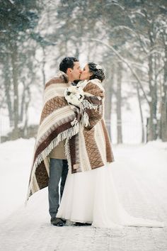 a bride and groom are kissing in the snow with a blanket draped over their heads