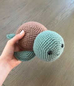 a hand holding a small crocheted turtle on top of a wooden floor next to a person's finger