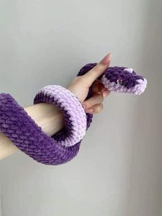 a hand holding a purple and white knitted snake