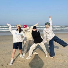 four people standing on the beach with their arms in the air and one person wearing a hat