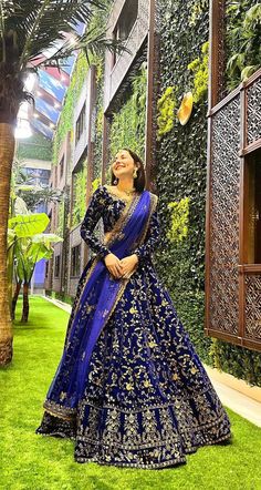 a woman in a blue and gold lehenga standing on grass with her eyes closed