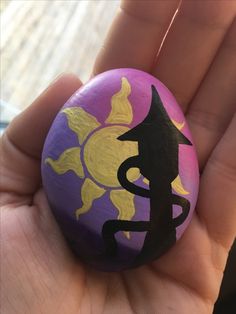 a hand holding a purple and yellow painted rock with an image of a cat on it