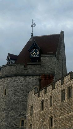 a clock on the side of a building with a weather vane in front of it