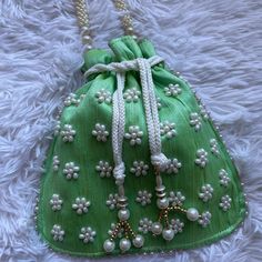 a green purse with white flowers and pearls on the front is laying on a furnishing