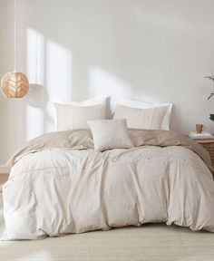 a bed with white linens and pillows in a room next to a potted plant