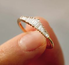 a woman's hand holding a gold ring with baguets on it,