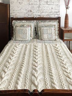 a bed with white blankets and pillows in front of a brick wall