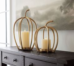 two candles sitting on top of a wooden table next to a wall with a painting behind it