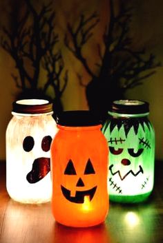 three mason jars with faces painted on them sitting on a wooden table in the dark