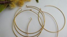 three pairs of gold hoop earrings sitting on top of a white table next to yellow flowers