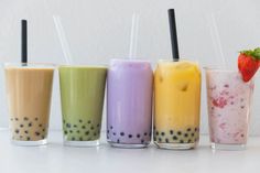 four different colored drinks with strawberries in them on a white countertop next to each other