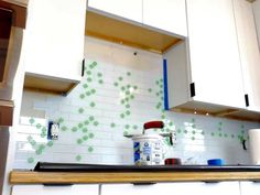 a kitchen with white cabinets and green dots on the backsplash