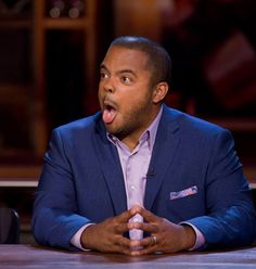 a man making a funny face while sitting at a table with his hands folded out