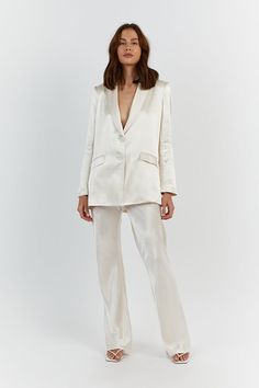 a woman standing in front of a white background wearing a white suit and matching heels