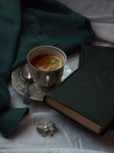 a cup of tea next to an open book on a bed with a green blanket