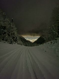 a snow covered road with trees on both sides and dark clouds in the sky above