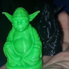 a green statue sitting on top of a person's hand next to a black object