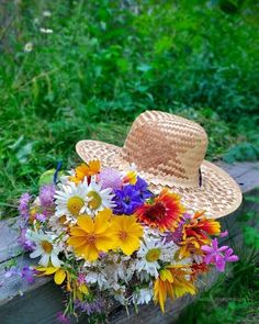 a straw hat sitting on top of a wooden bench filled with colorful wildflowers