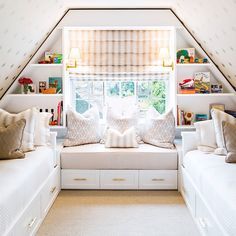 a bedroom with two white beds sitting under a window next to a shelf filled with books