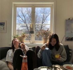 two people sitting on a couch with drinks in their hands and one person holding an orange juice bottle